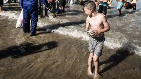 Getty Images A young boy holds caught sardines at the Amanzimtoti beach, south of Durban on July 3, 2019. - Like the running of the bulls in Spain, the migration of the wild-beast across Kenya, the sardine run along South Africa's East Coast is an annual event attracting thousands of locals and tourists. Each year massive shoals of sardines stretching hundreds of miles draw thousands of sharks, dolphins and gannets hovering above the fish. Masses of fishermen, locals line the shores to watch, catch and some sell them.