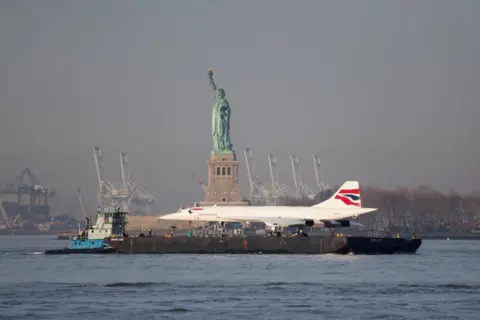 BRENDAN MCDERMID / REUTERS The Concorde supersonic jet is carried on a barge along the Hudson River past the Statue of Liberty
