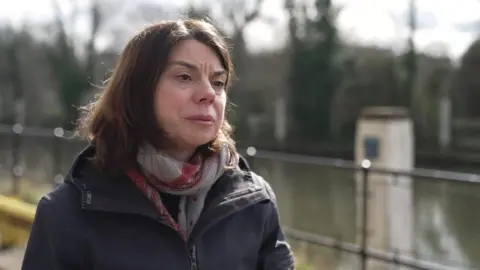 Image of Sarah Oley MP, wearing a dark jacket and red and white patterned scarf