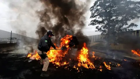 Reuters A member of the Federal Police removes a tire out of a burning barricade on BR-116 highway, during a protest against President Michel Temer in Sao Paulo, Brazil August 2, 2017.