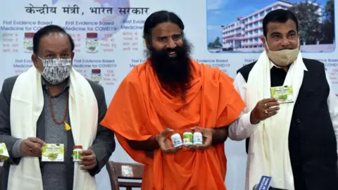 Getty Images Union Ministers Nitin Gadkari and Dr. Harsh Vardhan, Swami Baba Ramdev releases evidence based Patanjali Covid-19 Medicine Coronil during a press conference on February 19, 2021 in New Delhi, India. In June last year, Patanjali had launched 'Coronil and Swasari', what it claims is the Ayurvedic cure for treating Covid-19. Coronil has received the Certificate of Pharmaceutical Product (CoPP) from the Ayush section of Central Drugs Standard Control Organisation as per the WHO certification scheme," said Patanjali in a statement. (Photo by Sonu Mehta/Hindustan Times via Getty Images)