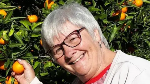 Jane Winn pictured picking oranges from a tree and smiling at the camera