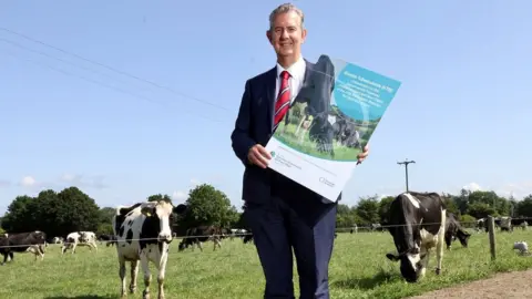 DAERA Agriculture Minister Edwin Poots holds a large copy of the bovine TB strategy plan in a cattle field at Cafre's Greenmount campus