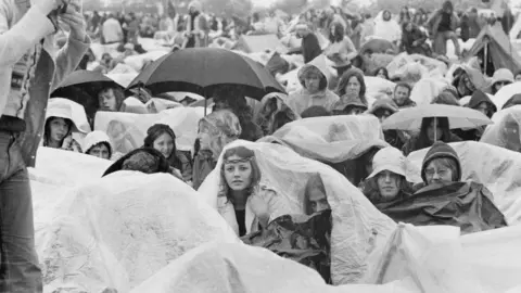 Getty Images Festival-goers shelter from the rain