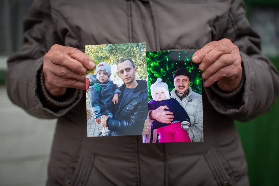 BBC Nadia Holumenkov holds pictures of her grandson Nikita and son Oleksandr