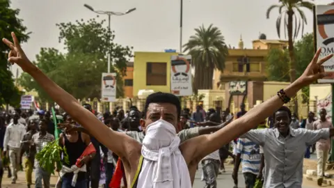 Getty Images A Sudanese protester covering his face with a jersey flashes the victory gesture while marching with others in a mass demonstration against the country's ruling generals in the capital Khartoum's twin city of Omdurman on June 30, 2019.