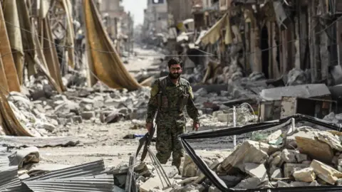 Getty Images A member of the Syrian Democratic Forces walks through the debris in the old city centre of Raqqa