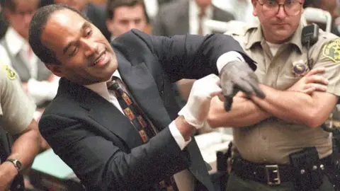 AFP/Getty Images Double murder defendant O.J. Simpson puts on one of the bloody gloves as a Los Angeles Sheriff's Deputy looks on during the O.J. Simpson murder trial 15 June. One of the gloves was found at the murder scene, while the other was found at Simpson's state.