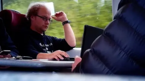 NCA Falder on the train using his laptop