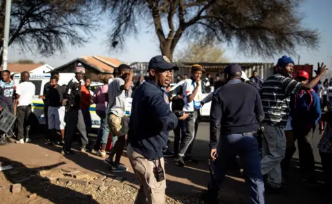 AFP South African police officers control the crowd in front of a looted foreign-owned shop in Soweto, Johannesburg,
