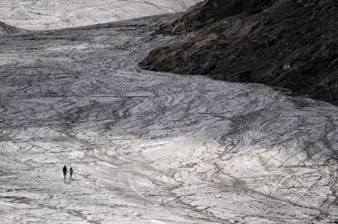 Fabrice Coffrini / AFP A couple hold hands while walking on the melting Tsanfleuron Glacier above Les Diablerets village in Switzerland on 6 August 2022