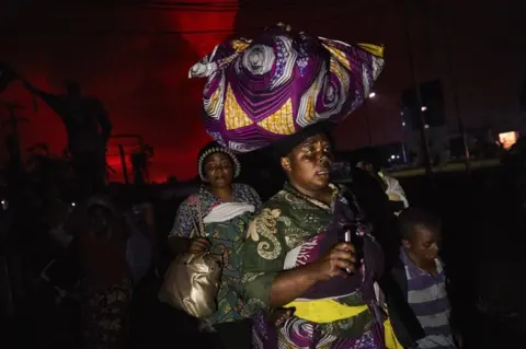 EPA A Congolese woman, carrying possessions on her head, flees from Mount Nyiragongo volcano as it erupts over Goma, Democratic Republic of the Congo, on 22 May 2021