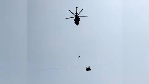 Army soldier slings down from a helicopter towards the cable