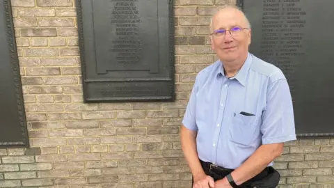 Justin Dealey/BBC David Cook in front of a war memorial in Luton, Bedfordshire