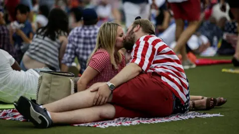 Getty Images A couple, dressed in US flag colours, kiss on a blanket on the grass