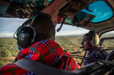 Georgina Smith/BBC Ambrose Ngetich and Captain Iltasayon Neepe look out from the cockpit of a helicopter