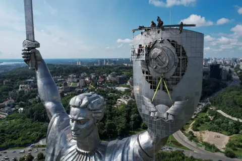 VALENTYN OGIRENKO/Reuters Workers dismount a Soviet emblem from the shield of the 'Motherland' monument, amid Russia's attack on Ukraine, at a compound of the World War II museum in Kyiv, Ukraine August 1, 2023.