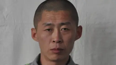 Jilin Police  North Korean prisoner Zhu Xianjian stands against grey backdrop
