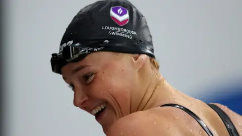 Getty Images Emily Crane smiling with her goggles on her forehead getting out the pool