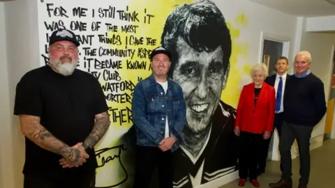 Watford FC Graham Taylor mural with people standing by it