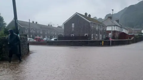 Luke Phillips/PA WIre Man in a raincoat walks alongside a flooded road in Port Talbot