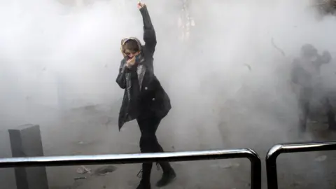 AFP An Iranian woman raises her fist amid the smoke of tear gas