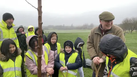 Schoolchildren alongside the lieutenant governor planting the first tree