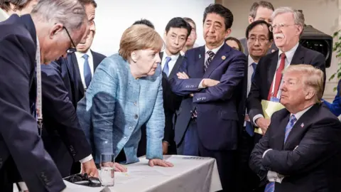 Getty Images In this photo provided by the German Government Press Office (BPA), German Chancellor Angela Merkel deliberates with US president Donald Trump on the sidelines of the official agenda on the second day of the G7 summit on June 9, 2018 in Charlevoix, Canada, looked on by other leaders.