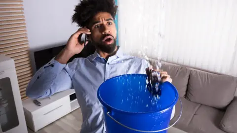 Getty Images A man holds a bucket under a leaking pipe