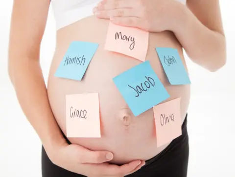 Getty Images A pregnant tummy with post it notes with baby names stuck all over it