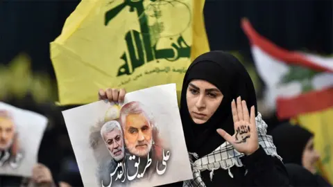 EPA Hezbollah supporter holds up a photo of Abu Mahdi al-Muhandis and Qasem Soleimani at a rally in Beirut, Lebanon (5 January 2020)