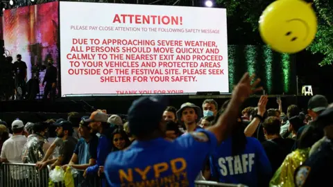 Reuters A screen shows information about severe weather approaching the area as New York police officers try to move people out of the field after cancelling the "We Love NYC: The Homecoming Concert" at Central Park