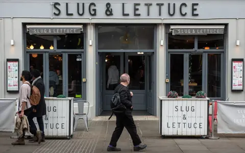 Getty Images A general view of a Slug and Lettuce bar and restaurant pub in the High Street on February 18, 2023 in Colchester, England. People with backpakcs are seen walking in front of the pub along the street.