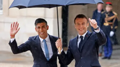 Getty Images Rishi Sunak and Emmanuel Macron smiling and gesturing to onlookers under an umbrella