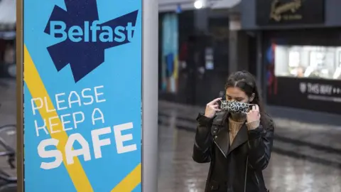 PA Media A woman puts a facemask on as she walks through Belfast city centre