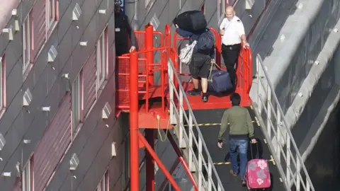 PA Media People boarding the Bibby Stockholm barge