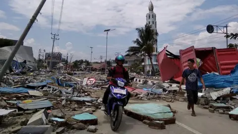 AFP/Getty Images Residents make their way along a street full of debris after an earthquake and tsunami hit Palu, Indonesia. Photo: 29 September 2018