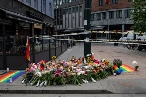 Rodrigo Freitas / Getty Images Flowers and rainbow flags are left along the street near the scene of a shooting in Oslo, Norway