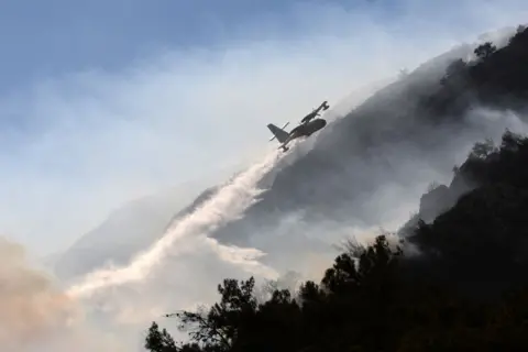 Getty Images A firefighting plane drops water over a wildfire forest fire which broke out in the Datça district of Mugla, Turkey