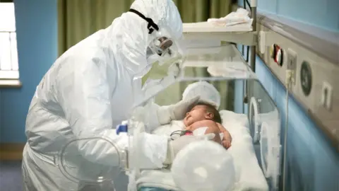 Reuters Doctor wearing PPE holding a baby