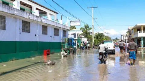 EPA Groups of people walk through a flooded street in Les Cayes
