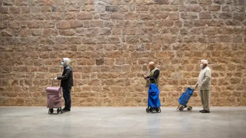 Getty Images People keep their distance as they wait their turn in a queue to access a Lidl supermarket in Barcelona