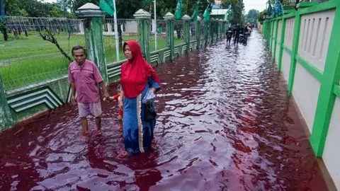 AFP Residents wade through floodwaters dyed red from the waste of a batik factory, a traditional textile product, in Pekalongan, central Java