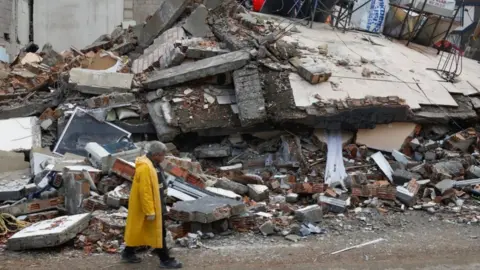 Reuters A man stands in front of a collapsed building, following an earthquake in Kirikhan, Hatay, Turkey