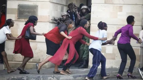 EPA Women are evacuated out of the scene as security officers search for attackers during an ongoing gunfire and explosions in Nairobi, Kenya, 15 January 2019.