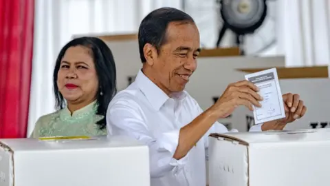 Getty Images Indonesian President Joko Widodo (R) and his wife Iriana cast their ballot during the presidential and legislative elections at a polling station at the State Administration Agency in Jakarta on February 14, 2024.