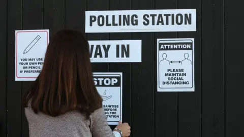 Reuters Woman putting up Covid signs on polling station