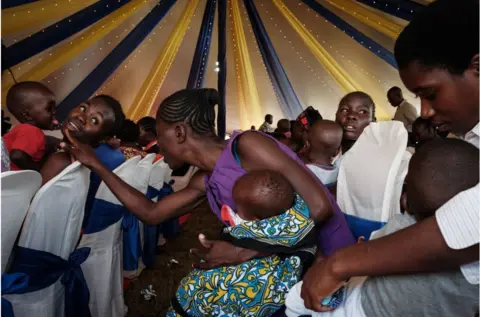 AFP Women carrying babies. One women in the centre wearing purple appears to be playing with a baby held by another person.