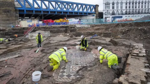 MOLA/Andy Chopping Archaeologists uncover the mosaic while a train bridge is in the background