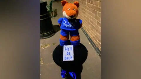 Syston Knitting Banxy Bollard topper featuring Filbert Fox with the words "We'll be back"